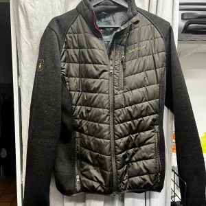 Svart quiltad jacka från Deerhunter - Säljer en svart quiltad jacka från Deerhunter med stickade ärmar och vadderad front och rygg. 