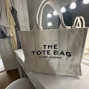 Beige shoppingväska Marc Jacobs - 'THE TOTE BAG' tryckt på framsidan. Väskan är i kraftig bomullscanvas, har både handtag och en bred axelrem samt innerfack med dragkedja. ‼️‼️INTE ÄKTA, köpt i Spanien aldrig använd