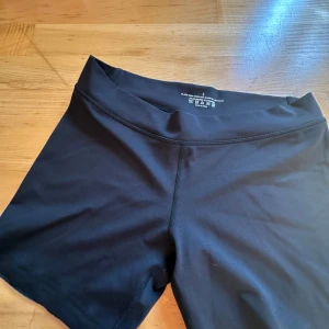 Svarta träningsshorts från Aim'n - Svarta, tighta träningsshorts från Aim'n med låg midja. Gjorda i stretchigt material (73% polyester, 27% spandex) och har silikonband på insidan av bensluten för att sitta på plats. Perfekta för gym eller löpning.