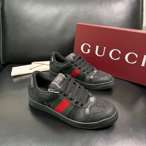 Svarta sneakers från Gucci med röd/grön detalj - Snygga svarta sneakers från Gucci med klassiska rödgröna ränder på sidorna och GG-logga framtill. Skorna har snörning, rund tå och är tillverkade i en mix av skinn och textil. Guldtext på hälen och diskreta detaljer gör dem riktigt stilrena.