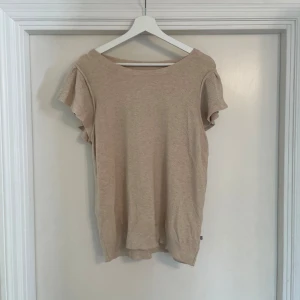 Beige blus med volangärmar - Snygg beige blus med korta volangärmar och rund halsringning. Toppens material känns mjukt och lätt, perfekt för en chill och stilren look. Passformen är normal och modellen är enkel men ändå trendig med de fina ärmdetaljerna.