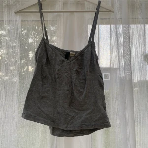 Grå linnetopp med smala axelband - En enkel och stilren grå linnetopp med smala axelband och v-ringning. Toppen är ärmlös och har en avslappnad passform, perfekt för varma dagar eller som lager under en skjorta. Tillverkad i mjuk bomull för en bekväm känsla.