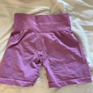 Ljuslila högmidjade shorts från NVGTN - Säljer ett par ljuslila högmidjade cykelshorts från NVGTN. De har bred ribbad midja för extra stöd och är tillverkade i ett stretchigt material som passar perfekt för träning. Snygg passform och stilren design utan synliga detaljer.