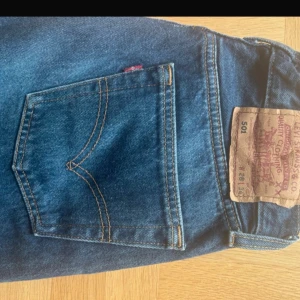Levi's 501 blå jeans straight fit - Klassiska Levi's 501 jeans i blå denim med raka ben och knappgylf. Snyggt tidlöst snitt och ikonisk läderpatch bak. Perfekta för dig som gillar en clean och autentisk jeanslook strl 28/34