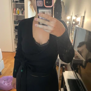 Svart omlott kofta i ribbstickad bomull - Säljer en svart ribbstickad omlottkofta med knyt i midjan. Koftan har v-ringning och långa ärmar, perfekt att slänga på sig över ett linne eller topp. Materialet är mjukt och stretchigt, vilket gör den både bekväm och snygg.