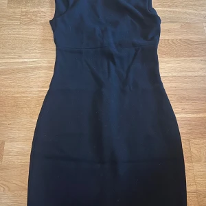 Svart kort klänning från Zara - Snygg svart ärmlös klänning från Zara Collection med figurnära passform och v-ringning. Klänningen har en dekorativ dragkedja framtill.