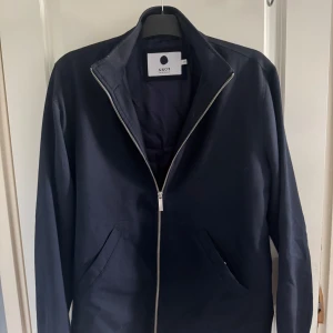 overshirt från NN07 - Snygg mörkblå overshirt från NN07 med minimalistisk design. Jackan har rak passform, hel dragkedja framtill och två snedställda fickor. Tillverkad i ett slitstarkt bomullstyg, perfekt för lager-på-lager-stil. Enkel ståkrage för en clean look.