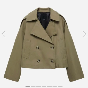 Grön trenchcoat från Mango - Säljer en grön croppad trenchcoat från Mango med dubbelknäppning och bred krage. Nypris 750 kr! Jackan har långa ärmar, axelklaffar och två fickor framtill. Jackan är använd några få gånger och är i super fint skick🩷