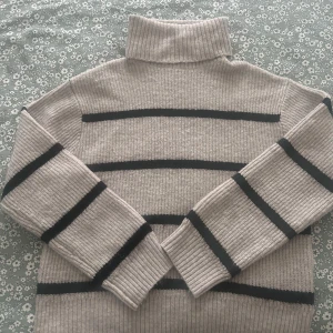 Beige randig stickad tröja - Säljer en ribbstickad beige polotröja från H&M med svarta horisontella ränder. Tröjan har hög polokrage och långa ärmar, perfekt för lager-på-lager. Mjuk och skön, passar dig som gillar en chill och stilren vibe.