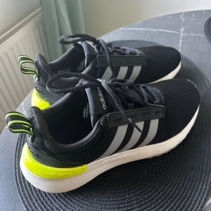 Adidas Cloudfoam sneakers svart/gul - Svarta Adidas Cloudfoam sneakers med vita och neongula detaljer. Skorna har klassiska tre ränder på sidan, snörning och en bekväm Cloudfoam-sula. Ovandelen är i textil och sidorna har gråa ränder. Sulan är vit med svarta och gula inslag undertill.