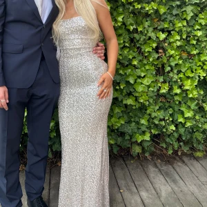 Glittrig långklänning i silver - Säljer nu min superfina balklänning från BabyBooFashion i storlek xs. Så smickrande passform och lite stretchig i material så sitter perfekt. Jag är själv ca 160 lång och den passade perfekt i längden när jag hade 8 cm klackar. Endast använd en gång och därför i perfekt skick. Följer med en rosett (se sista bilden) som går att sätta fast i ryggen. 