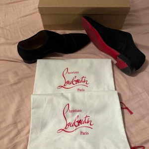 Svarta mockaskor från Christian Louboutin - Snygga svarta mockaskor från Christian Louboutin med ikonisk röd sula. Skorna har en elegant, spetsig tå och låg klack. Perfekta för dig som vill sticka ut med exklusiv design och lyxig känsla. Kommer med originalpåse och box och även sulskydd som jag inte har med på bilden. Pris kan diskuteras 