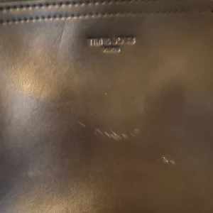 Svart axelväska från Tim & joss - Snygg svart axelväska från Tim & Joss slätt skinn. Väskan har två stora fack med dragkedjor och en justerbar axelrem i samma material. Perfekt storlek för det viktigaste och stilren design som funkar till allt. Dock lite skador men inget man märker 