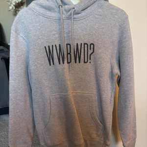 Grå hoodie ”What Would Blair Waldorf Do?” - Säljer en stilren grå hoodie med svart texttryck. Tröjan har huva med snörning, ficka och långa ärmar. Perfekt för chill dagar eller när du vill ha en enkel men snygg look.
