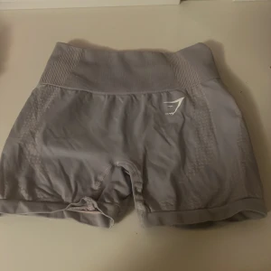Ljuslila Gymshark shorts - Snygga grå seamless shorts från Gymshark med hög midja och ribbad linning. Materialet är stretchigt syntet och har ventilerande detaljer längs sidorna. Perfekta för gymmet eller annan träning, med diskret logga framtill.