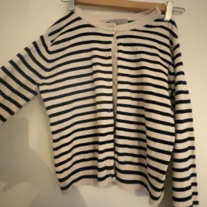 Fin Randig kofta från H&M i bomull  - Säljer en snygg randig kofta från H&M i storlek S. Den är vit med svarta horisontella ränder, har långa ärmar och knappar framtill. Materialet är mjuk bomull som känns skönt mot huden. Perfekt för dig som gillar klassisk stil med en twist.
