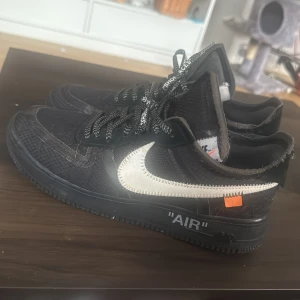 Nike Air Force 1 x Off-White svart - Nike Air Force 1 x Off-White i svart med vit, broderad swoosh och orange detalj. Skorna har mesh och syntetmaterial, platt sula och rund tå. Svarta och vita snören med texten 'SHOELACES' och tydliga Off-White detaljer. Perfekt för dig som gillar streetwear. Zip-tie finns inte och har slitage från daglig användning därav priset. Från Monicasneaker