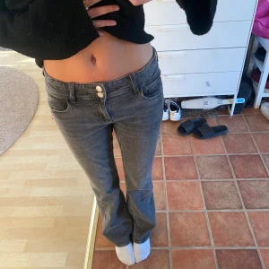 Grå jeans från Gina Tricot - Säljer ett par grå jeans från Gina Tricot med raka ben och två knappar i midjan. Jeansen har klassiska fickor fram och bak, varav bakfickorna har lock och knapp. Perfekta till en chill vardagslook.