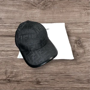 Svart keps från Fendi med mönster - Snygg svart keps från Fendi med diskret FF-logomönster över hela kepsen. Klassisk form med böjd skärm och justerbar baksida. Materialet har en lätt glansig finish som ger en exklusiv känsla. Perfekt för dig som gillar designeraccessoarer.