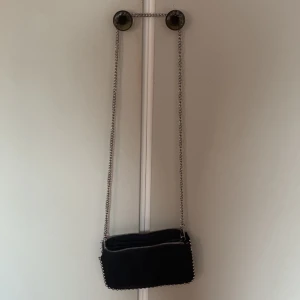 Svart mocka axelväska från Zara - Snygg svart axelväska i mocka från Zara med silverfärgad kedja och dragkedja. Väskan har flera fack inuti för att hålla ordning på dina grejer. Perfekt storlek för mobilen och det viktigaste.