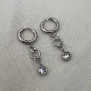 Silvriga örhängen med kedja och sten - Snygga silvriga örhängen med rund form och hängande kedja. Längst ner sitter en glittrande klar sten som ger extra bling. Perfekta för dig som gillar minimalistisk stil med en touch av sparkle. Rostfritt stål. 