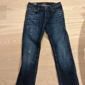 Mörkblå Replay jeans med slitningar - Snygga mörkblå jeans från Jack and Jones med slitna detaljer och lätt tvättade partier. Klassisk femficksmodell med raka ben och låg midja. Jeansen har en cool, använd look och är tillverkade i mjukt denimtyg. Jag har själv gjort slitningarna. Dem är använda men väldigt bra skick har växt ut dem, använde dom i sen maj ungefär och väldigt bra skick.