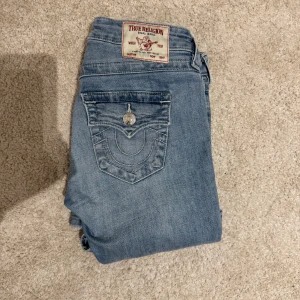True Religion ljusblå bootcut jeans - Ljusblå jeans från True Religion med bootcut passform och klassiska kontrastsömmar. Snygga fickdetaljer med lock och silverknappar bak samt ikonisk patch i midjan. **((Dem är uppsydda för personer under 160))**🌸