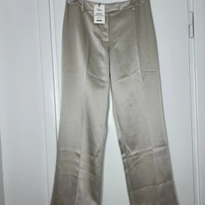 Champagnefärgade kostymbyxor BikBok (M/L - Snygga champagnefärgade kostymbyxor från BikBok i glansig polyester. Byxorna har raka ben, pressveck och hällor för bälte. Det passar om du använder Medium