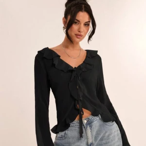 Svart blus med volang och knyt - Svart blus med långa ärmar, volangdetaljer längs v-ringningen och knyt framtill. Nyskick från SHEIN.