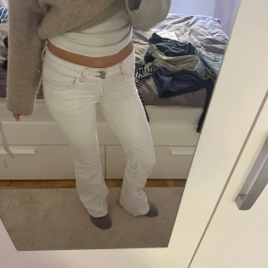 Vita bootcut jeans från Nelly - Säljer ett par vita bootcut jeans från Nelly med snygga kontrastsömmar i beige. Byxorna har låg midja och klassisk femficksdesign. Materialet är stretchigt och bekvämt, perfekt för dig som gillar en stilren look med lite 00-talsvibe. Jag är 173 cm lång och köpte jeansen för 699kr