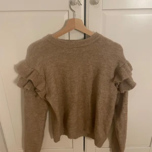 Beige stickad tröja H&M - Superfin beige stickad tröja från H&M med volangdetaljer på axlarna. Tröjan har rund halsringning och långa ärmar, perfekt för att ge outfiten en söt och trendig touch. Passar s m men är i 170