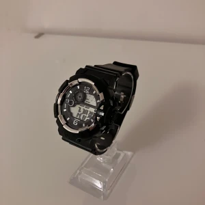 Svart digital sportklocka - Cool svart digital sportklocka med robust design och silverfärgade detaljer runt urtavlan. Klockan har både digital och analog visning, svart plastarmband och flera funktioner som datum och veckodag. Perfekt för dig som gillar en sportig och modern stil.                                      ✅Frakt inom 24 timmar 📦.                                                         ✅Nytt batteri 🔋.    