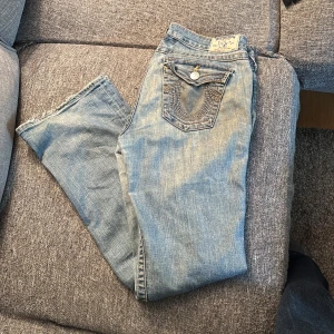 True Religion ljusblå bootcut jeans - Säljer ett par ljusblå jeans från True Religion med klassiska kontrastsömmar och snygga detaljer på bakfickorna. Jeansen har bootcut-modell med low rise. W32