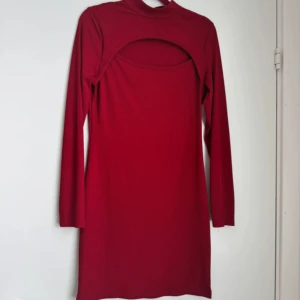 Röd långärmad klänning med cut out - Trendig röd kortklänning med lång ärm och cool cut out-detalj över bröstet. Hög hals och figurnära passform gör den perfekt för dig som vill sticka ut. Mjuk och stretchig i materialet, superenkel att styla med boots eller sneakers.