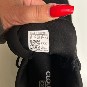 Svarta Adidas Cloudfoam sneakers - Säljer ett par helsvarta Adidas Cloudfoam sneakers med klassiska tre ränder på sidan. Skorna har snörning, rund tå och en mjuk, dämpad sula för extra komfort. Ovandelen är i textil och syntet, perfekt för dig som gillar stilrena och bekväma sneakers.