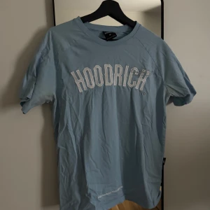 Ljusblå HOODRICH t-shirt - Snygg ljusblå t-shirt från HOODRICH med vit broderad logga framtill. Klassisk rund hals och korta ärmar. Perfekt för en chill streetwear-look. Tillverkad i mjuk bomull för skön känsla hela dagen.