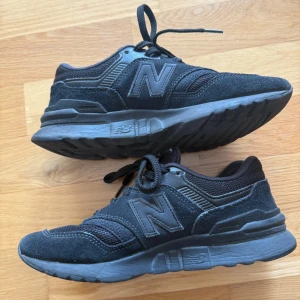 Svarta New Balance sneakers - Snygga svarta New Balance sneakers med klassisk N-logga på sidan. Skorna har en mix av mocka och mesh, vilket ger både stil och bra andningsförmåga. Tjock sula för extra komfort och snörning framtill. 