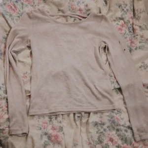 Ljusrosa stickad tröja med snörning i ryggen - Beige ljusrosa tröja i storlek S med lång ärm och snygg snörningsdetalj i ryggen. Tröjan har en djup v-ringning bak och är i mjukt material. Perfekt för lager-på-lager och passar till både jeans och kjol.