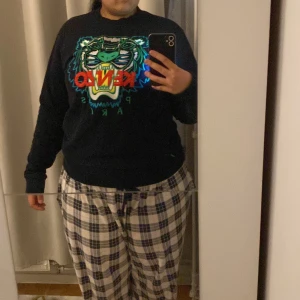 Svart Kenzo sweatshirt med tiger - Svart sweatshirt från Kenzo med ikoniskt broderat tigerhuvud i blått, grönt och silver samt röd Kenzo-logga framtill. Tröjan har rund hals, långa ärmar och ribbade muddar. Perfekt statement piece för dig som vill sticka ut.