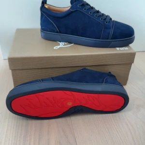 Mörkblå sneakers från Christian Louboutin - Snygga mörkblå sneakers från Christian Louboutin i mocka med klassisk röd sula och diskreta detaljer. Skorna har rund tå, snörning och platt sula. Perfekta för dig som vill sticka ut med exklusiv stil och ikonisk design. Storlek 41. Fick den som en present men den är för liten för mig