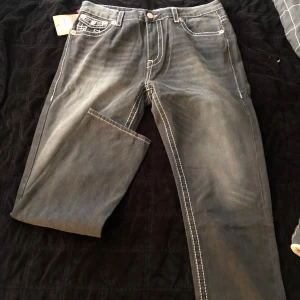  Herr Svarta jeans från True Religion - Säljer ett par svarta jeans från True Religion med tydliga vita kontrastsömmar och ikoniska bakfickor med broderad logga. Jeansen har klassisk femficksdesign och raka ben. Perfekta för dig som vill sticka ut med detaljer.