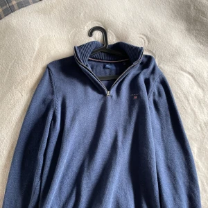 Marinblå stickad tröja från Gant - Snygg marinblå stickad tröja från Gant med halv dragkedja och ribbad krage. Tröjan har broderad Gant-logga på bröstet och långa ärmar. Perfekt för lager-på-lager och chillare dagar.