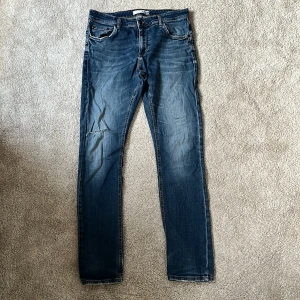 Blå jeans från Visual Clothing Project - Snygga vanliga blå jeans från Visual Clothing Project med klassisk femficksdesign och slitning på vänster knä. Jeansen har raka ben och normal passform, tillverkade i mjukt denimtyg med orange kontrastsömmar. Perfekta för en avslappnad stil. Otroligt bra pris för jeansen! Storlek W33/L32