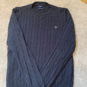 Mörkblå kabelstickad tröja från Gant - Säljer en mörkblå kabelstickad tröja från Gant i 100% bomull. Tröjan har rund halsringning, ribbade muddar och Gant-logga broderad på bröstet. Perfekt för dig som gillar klassisk och stilren look.                                                                                    Kontakta mig vid funderingar samt frågor och ge prisförslag 