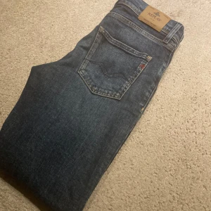 Mörkblå jeans från Replay Wallys - Snygga mörkblå jeans från Replay, modell Wallys. Klassisk femficksdesign med guldfärgade sömmar och läderpatch bak i midjan. Jeansen är tillverkade i slitstarkt denim och har en rak passform som funkar till det mesta.