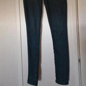 Svarta skinnybyxor med dragkedja bak - Svarta byxor med tight passform och hög midja. Snygg detalj med dragkedja bak och två bakfickor. Dom är välanvända vilket syns genom att färgen blivit blekt i tvätt och att tyget är slitet (se bilder). Stl M/L