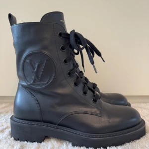 Svarta boots från Louis Vuitton - Knappt använda. Kvitto finns från Louis Vuitton butiken i Sthlm. Snygga svarta boots från Louis Vuitton i skinn med grov sula och snörning framtill. Ikonisk LV-logga på sidan och präglad blomdetalj baktill. Tjock platt sula och rund tå ger en cool och robust look. Perfekta för dig som vill sticka ut med lyxiga detaljer. 