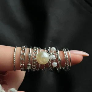Set med 10 silverfärgade ringar med pärlor - Säljer ett snyggt set med tio silverfärgade ringar i olika stilar. Några har kedjedetaljer, andra är släta eller tvinnade, och två har vita pärlor som hänger eller sitter fast. Perfekt för att mixa och matcha på flera fingrar för en cool look.
