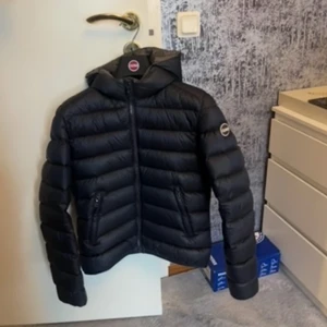 Svart Colmar dunjacka med huva - Säljer en mörkblå dunjacka från Colmar med huva och dragkedja framtill. Jackan har en quiltad design, två fickor med dragkedja och Colmar-logga på ärmen. Perfekt för kalla dagar och riktigt snygg till streetwear-stilen. Den är köpt för 4999kr och är i storlek c34/ motsvarar s den har en liten repa som man kan se på bild 3 men den syns inte på annars är den hel och är i ett jätte fint skick, har även prislappen kvar och galjen medföljer ❤️