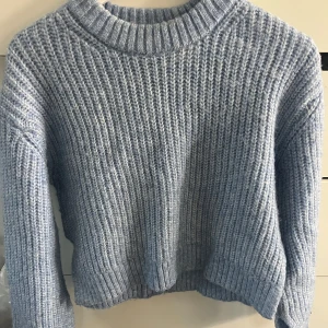 Stickad croppad tröja i blått och grått - Två mysiga stickade tröjor i croppad modell, en i ljusblå och en i ljusgrå. Båda har grov ribbstickning, rund halsringning och långa ärmar. Perfekta för lager-på-lager under kyliga dagar.